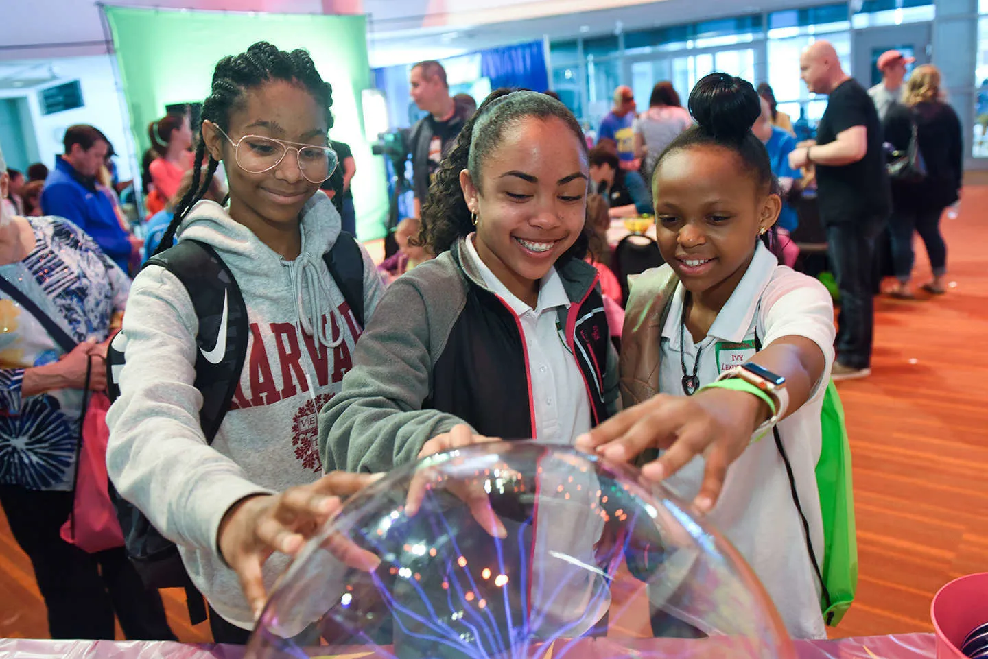 Three girls reach their hands out to a glass ball with visible electricity streams