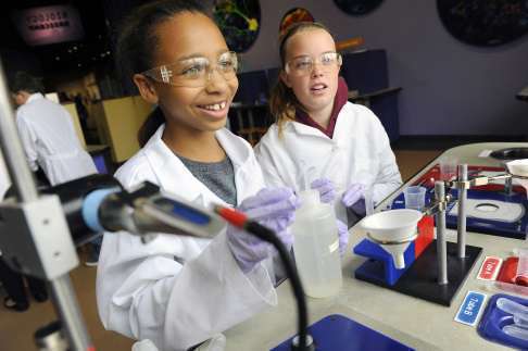 Two students exploring wearing white lab coats and purple gloves complete a science experiment in Expedition Health