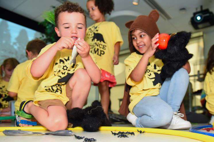 Two children wearing yellow shirts are seated on the floor, happily playing with an assortment of stuffed animals around them.