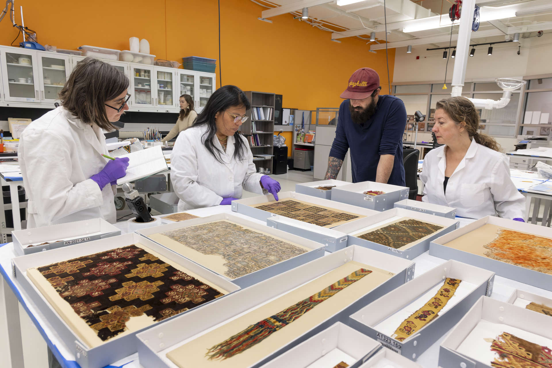 Three women and one male researcher look at Archeological Textiles in the laboratory