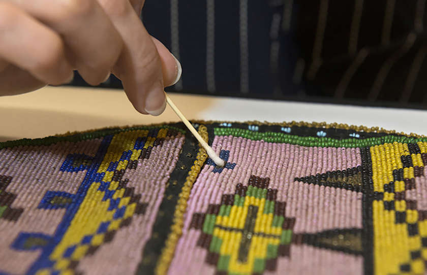 close up of a conservator using a Q-tip to clean a colorful beaded object