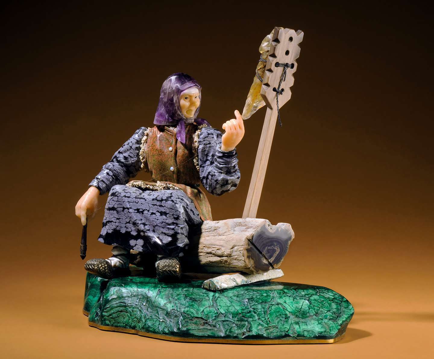 Gem carving called "The Grandmother": statue of a woman seated on a log, made of quartz, amethyst, obsidian, jasper, aragonite, gold plated silver, malachite, and petrified wood.